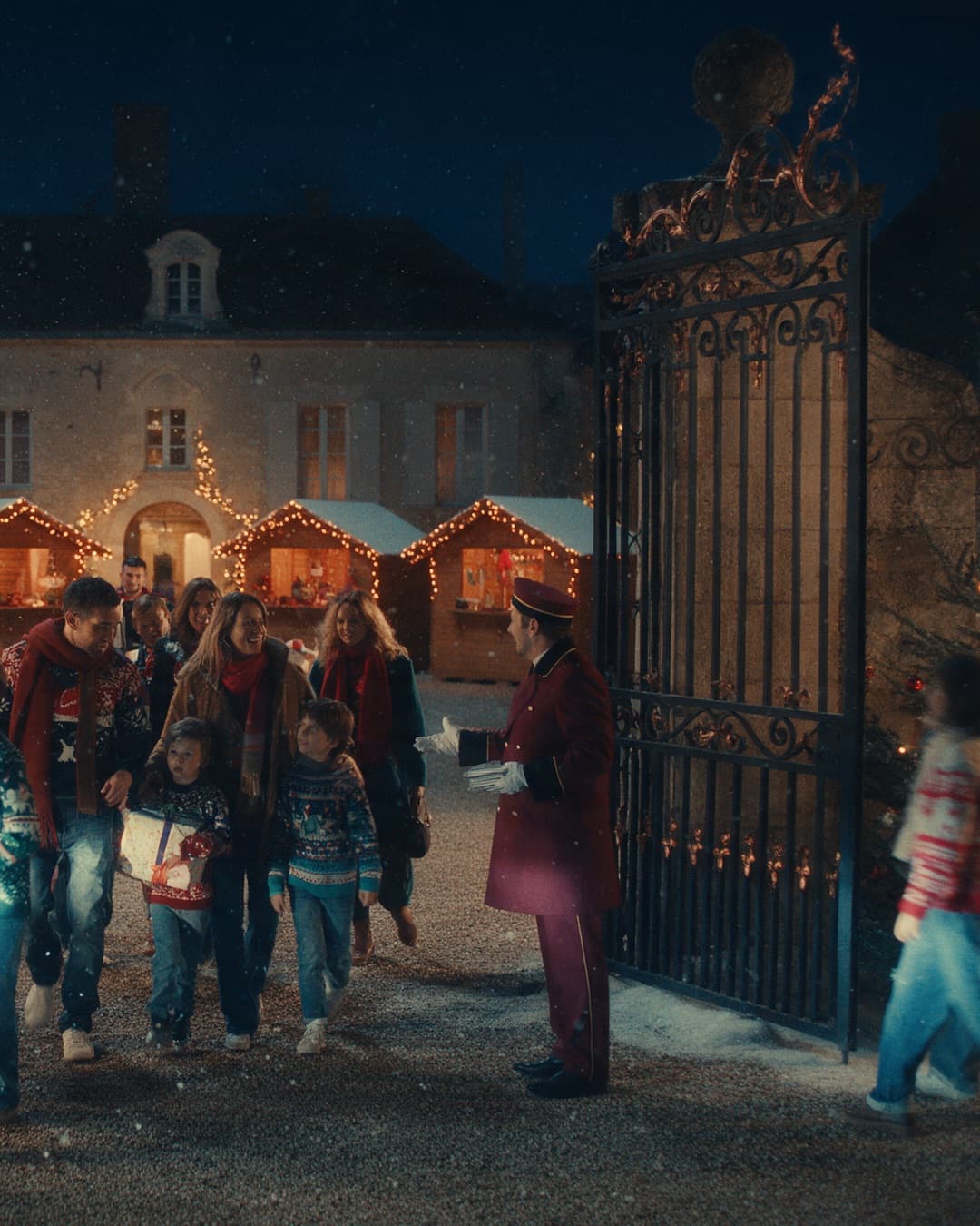 Une bande de collègues et d’enfants en pulls de Noël franchit de nuit le portail du Domaine les 12 Ponts, descendue d’un bus et accueillie par un groom en tenue bordeaux devant quatre chalets éclairés.